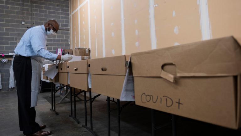 Mortician and funeral director Bryan Clayton inspects names on a row of cardboard caskets, one reading "COVID+," at Maryland Cremation Services in Millersville, Md.