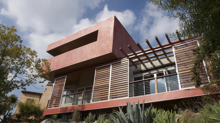 Photo of a modern house with movable wooden slat panels to shade large exterior windows.