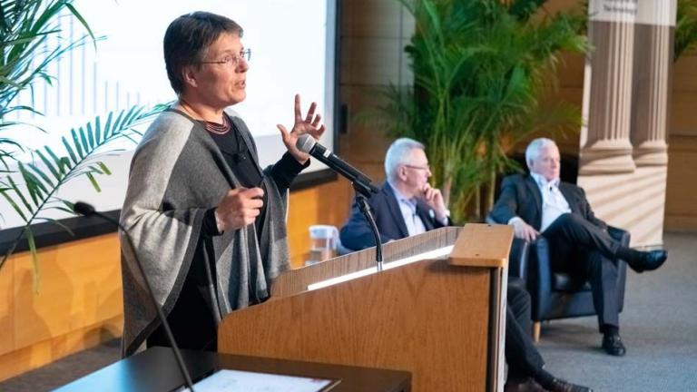 Susanne Moser, director of Susanne Moser Research and Consulting, addresses MIT’s second Symposium on Climate Change. In the background are Andrew Steer, president and CEO of the World Resources Institute, and Richard Schmalensee, the Howard W. Johnson Professor of Management and Professor of Economics Emeritus at the MIT Sloan School of Management, who moderated the panel discussions.