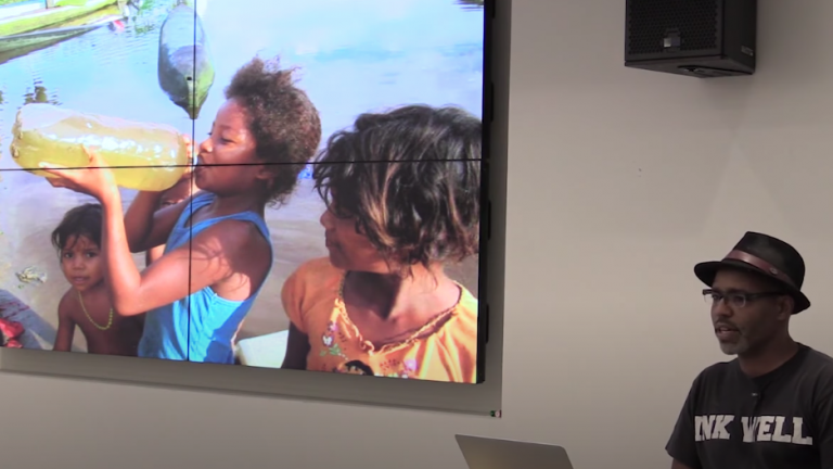 Photo of Professor Carpenter speaking about an image of young children drinking from a plastic bottle filled with polluted water.