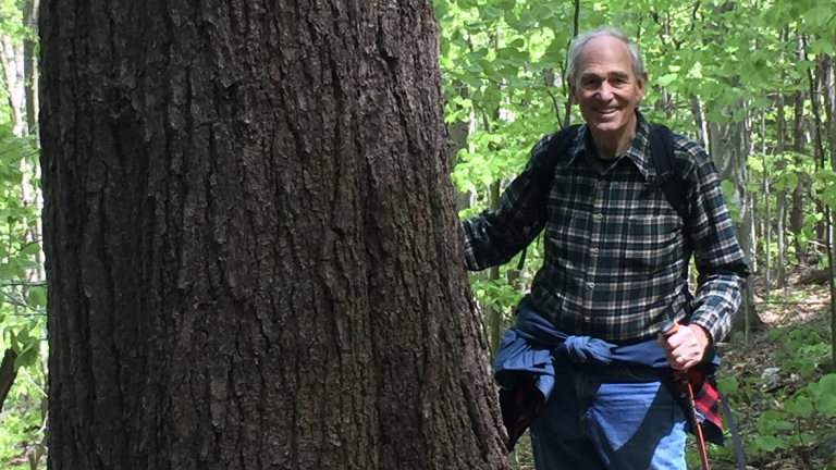 William Moomaw PhD ’65 stands next to a large tree while hiking in the woods