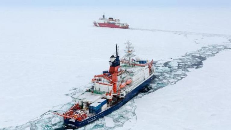 An icebreaker and Coast Guard cutter travel through a channel in the ice of the Arctic Ocean