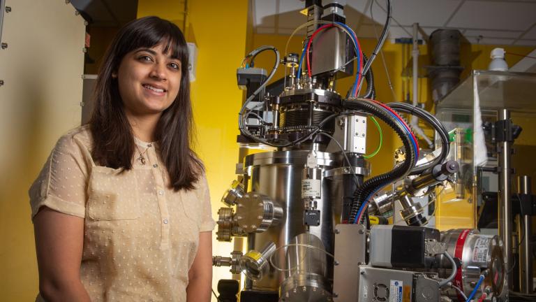 Postdoc Reshma Rao stands next to a pulsed laser deposition system, which is used to deposit well-defined thin films of catalyst materials. 