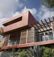 Photo of a modern house with movable wooden slat panels to shade large exterior windows.