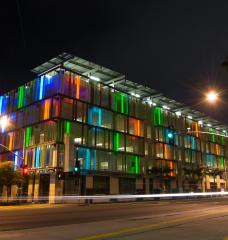 The exterior of a modern, glass-clad parking garage, lit up at night with different colors shining out.