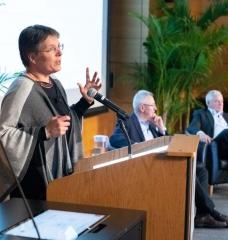 Susanne Moser, director of Susanne Moser Research and Consulting, addresses MIT’s second Symposium on Climate Change. In the background are Andrew Steer, president and CEO of the World Resources Institute, and Richard Schmalensee, the Howard W. Johnson Professor of Management and Professor of Economics Emeritus at the MIT Sloan School of Management, who moderated the panel discussions.