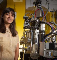 Postdoc Reshma Rao stands next to a pulsed laser deposition system, which is used to deposit well-defined thin films of catalyst materials. 